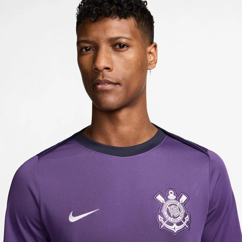 Detalhe do escudo bordado da Camisa Corinthians Treino 25/26 Nike Masculina, símbolo do Timão, que exibe sua paixão pelo clube.